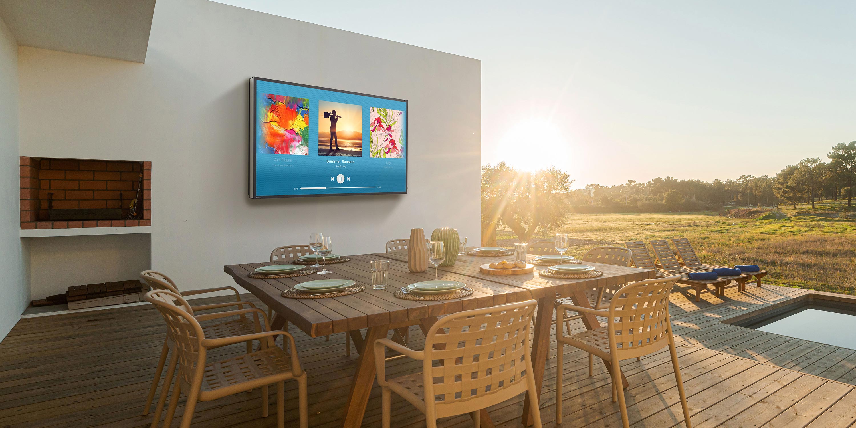 Outdoor dining area with a mounted TV, overlooking a scenic sunset view.