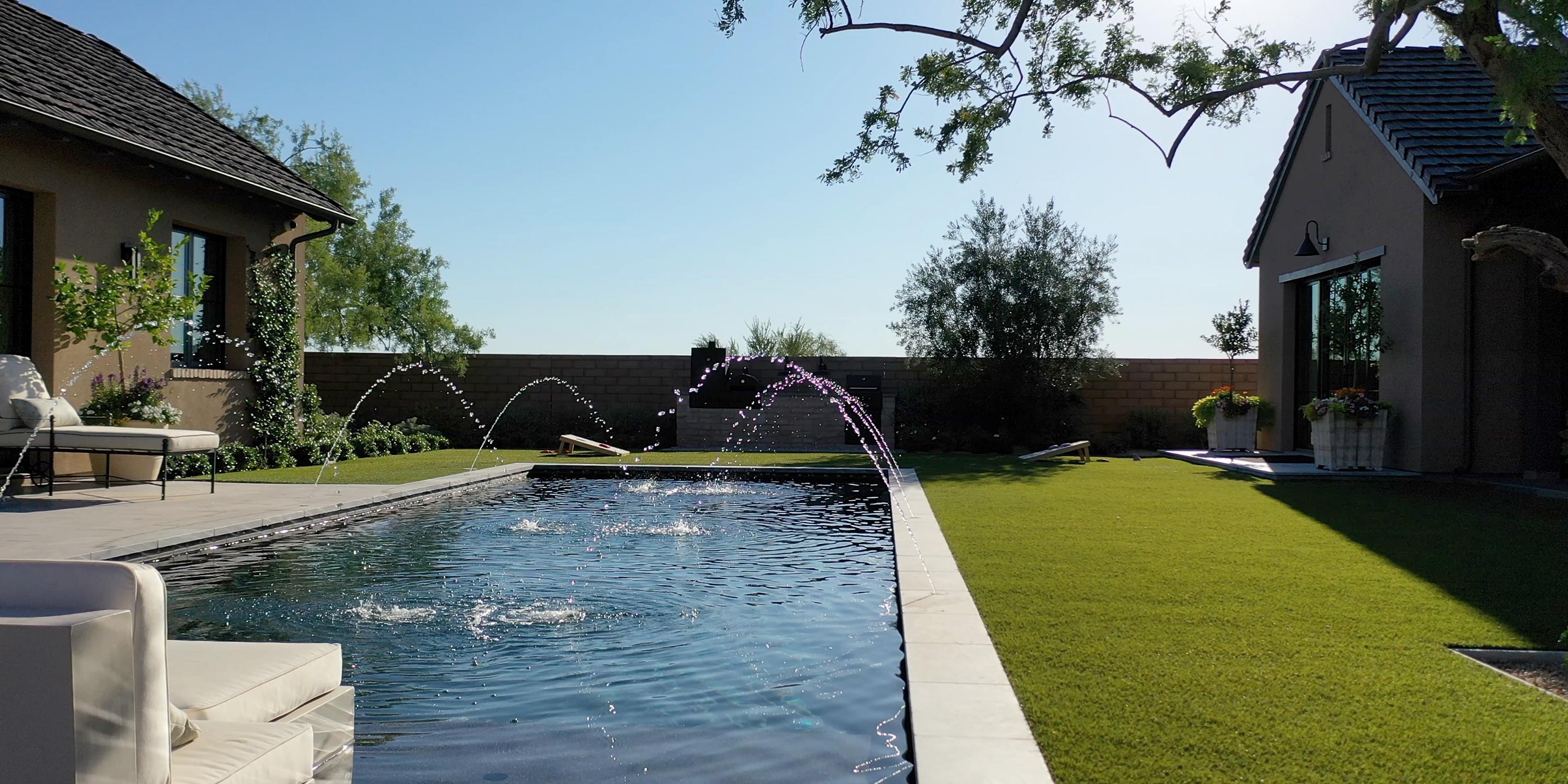 Backyard pool with elegant water fountains and lush green surroundings.