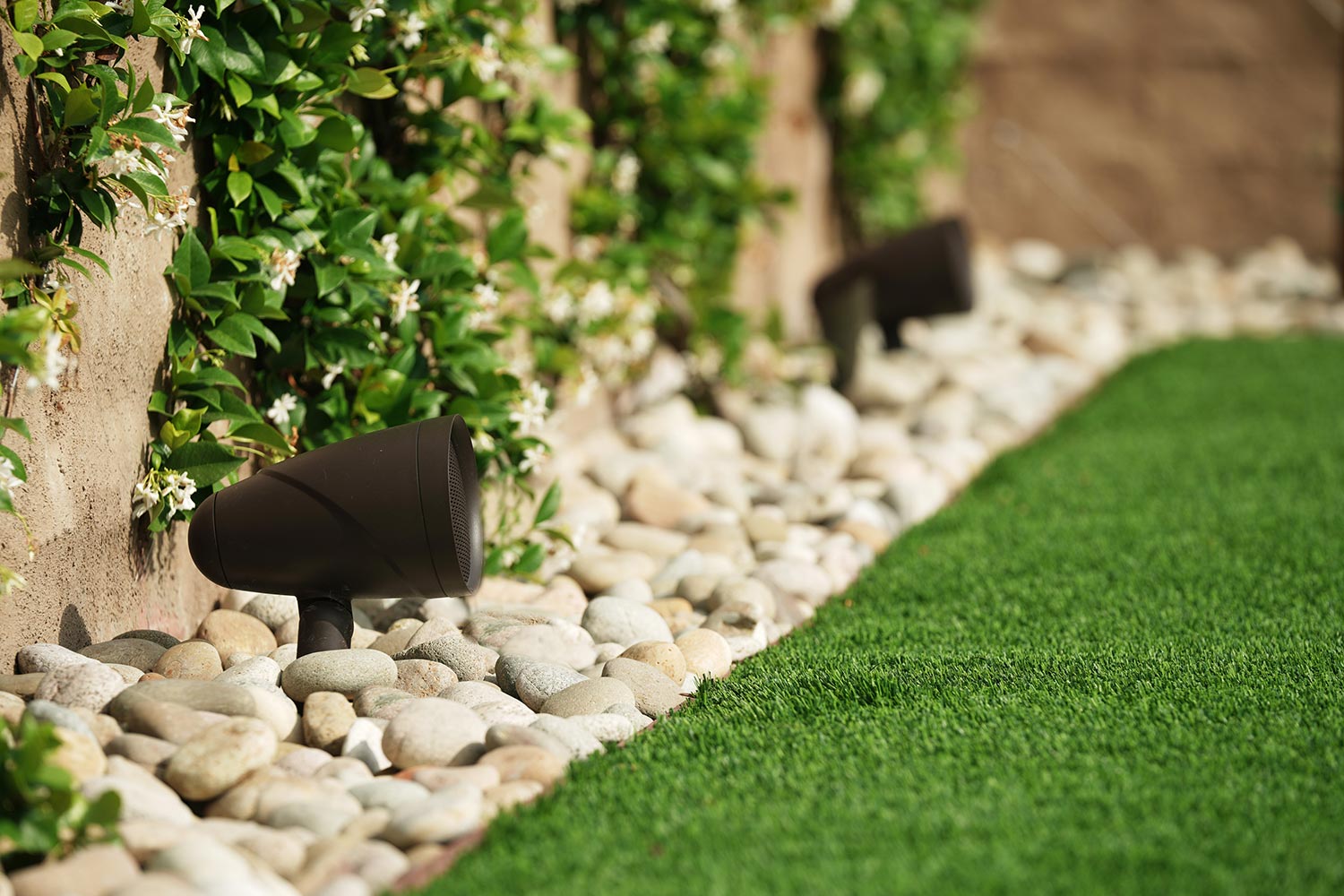 Garden landscape with brown outdoor speaker surrounded by pebbles and greenery