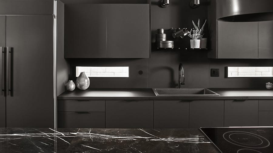 Modern black kitchen with sleek cabinets, a marble countertop, and minimalistic decor.