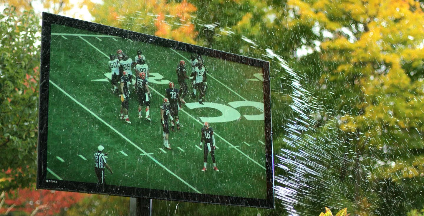 Outdoor TV showing a football game while being sprayed with water.