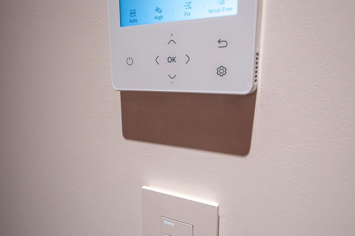 Wall-mounted thermostat above a labeled lighting control panel